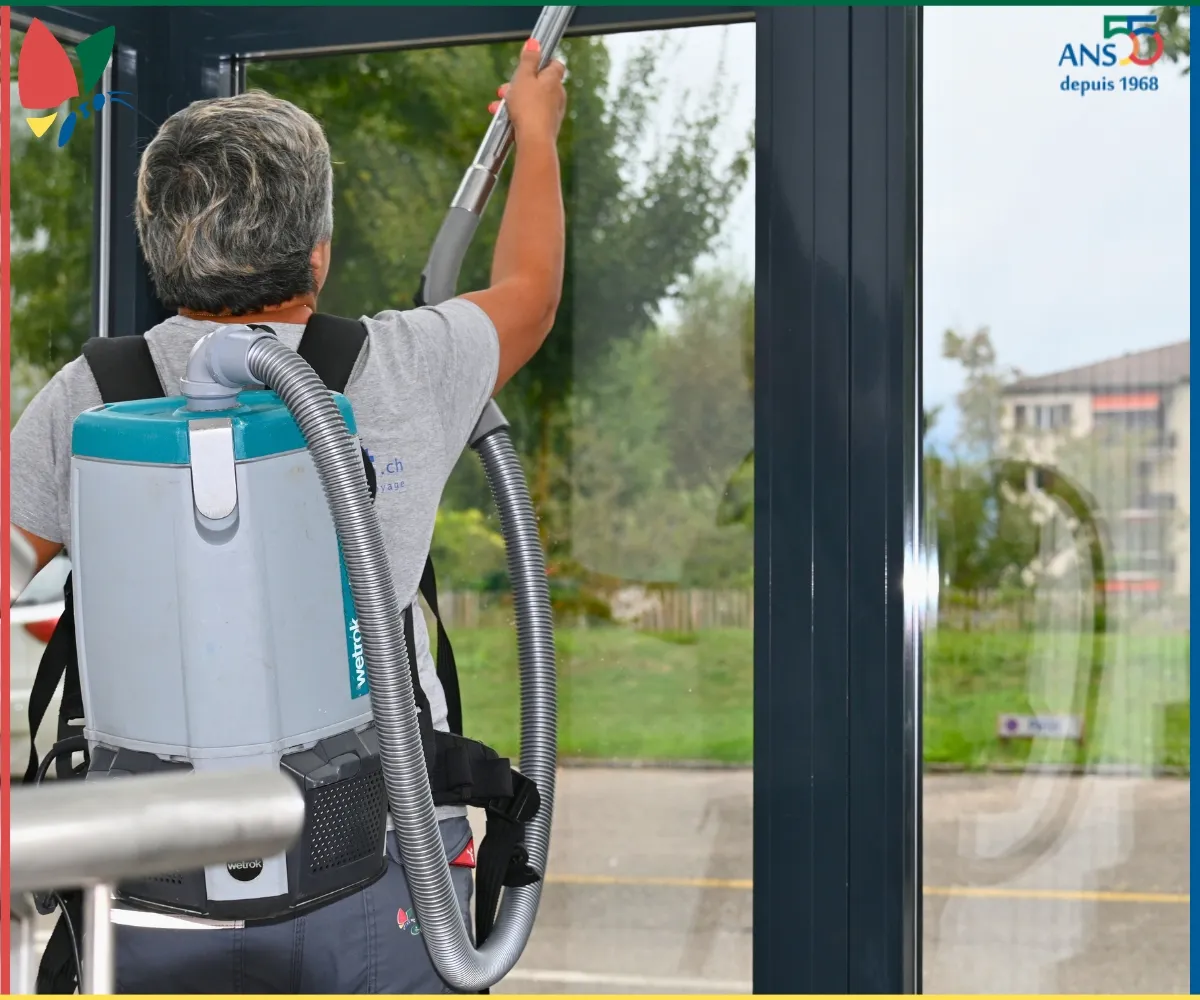 Collaboratrice équipée d’un aspirateur dorsal intervenant sur l’encadrement d’une porte vitrée.