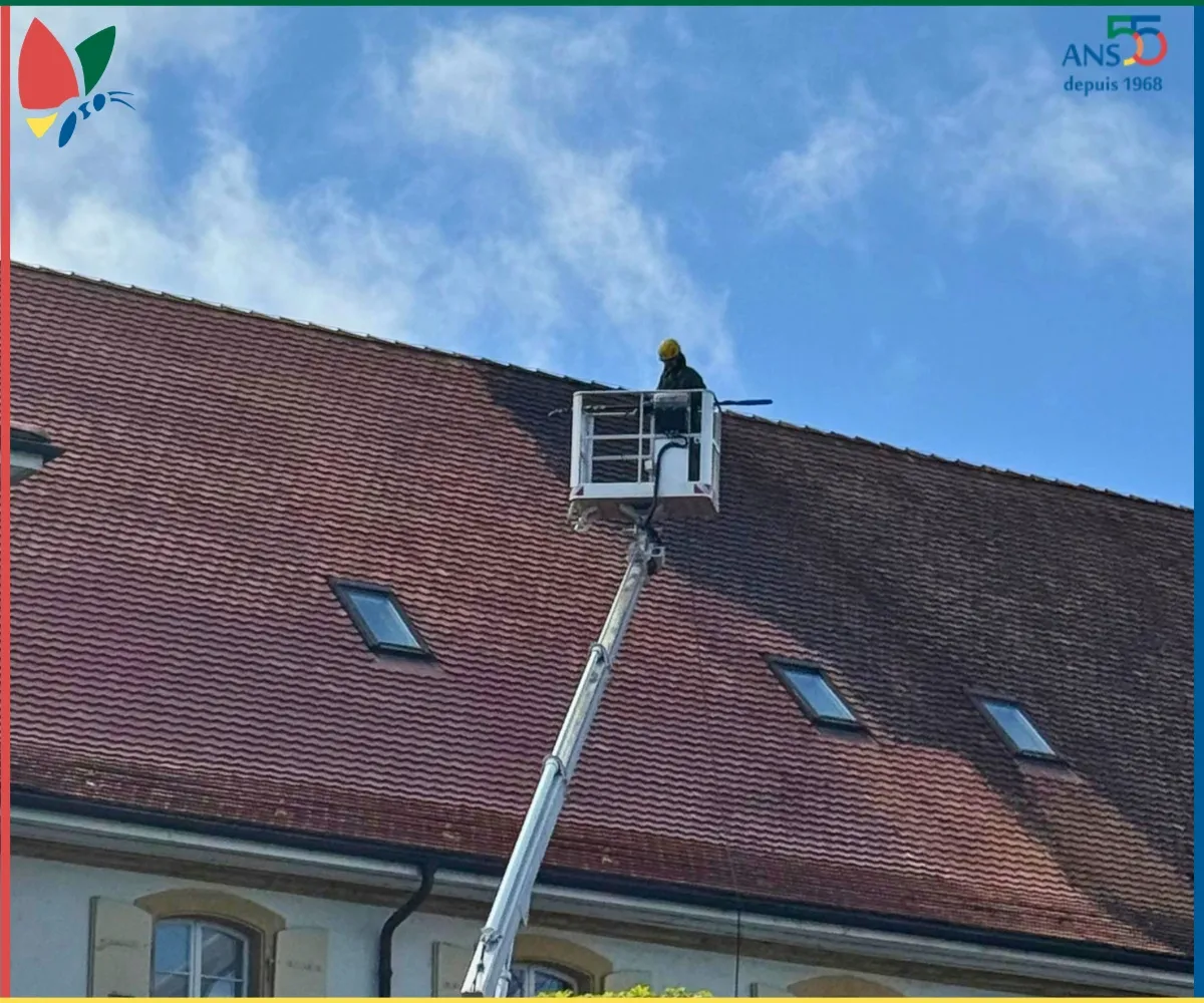 Technicien intervenant depuis une nacelle pour nettoyer une toiture en tuiles.