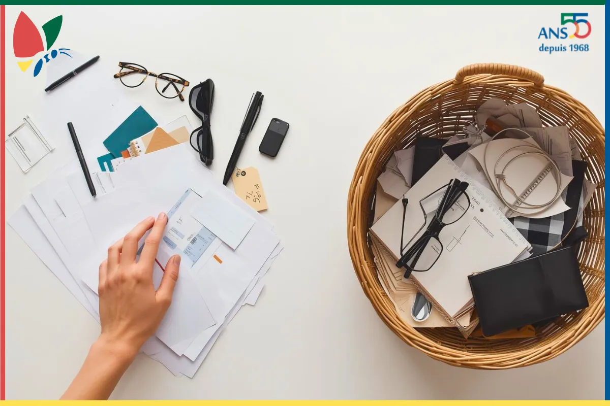 Tri de documents et d’objets du quotidien, avec une main en train de désencombrer un bureau avant de les placer dans un panier de rangement
